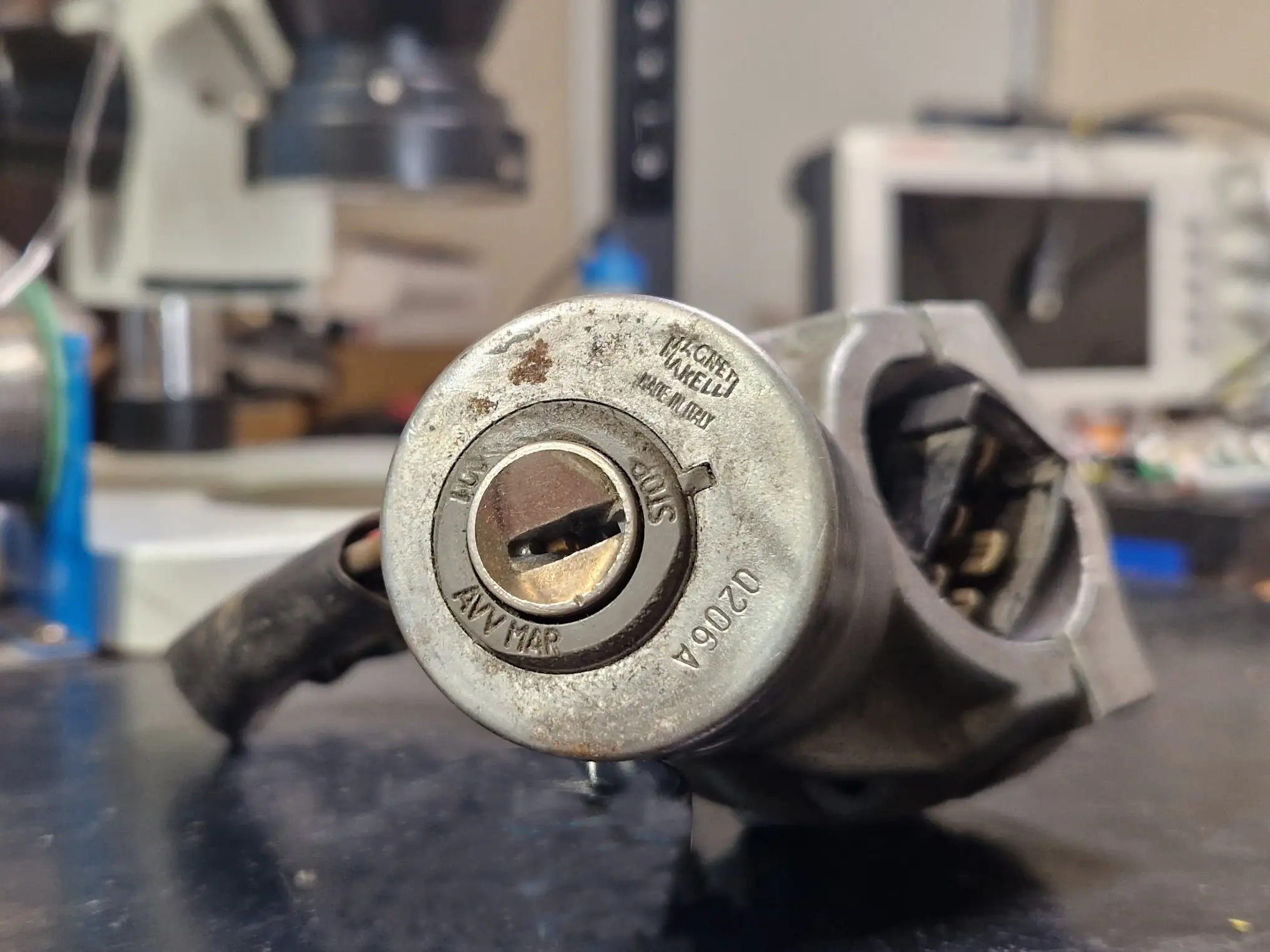 Ausgebautes Magneti Marelli Zündschloss vor einem Reparaturmikroskop in der Werkstatt von Schlüsseldienst Aigner.